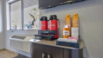A kitchenette with a Bunn coffee maker, two red dispensers, and a stack of yellow cups.