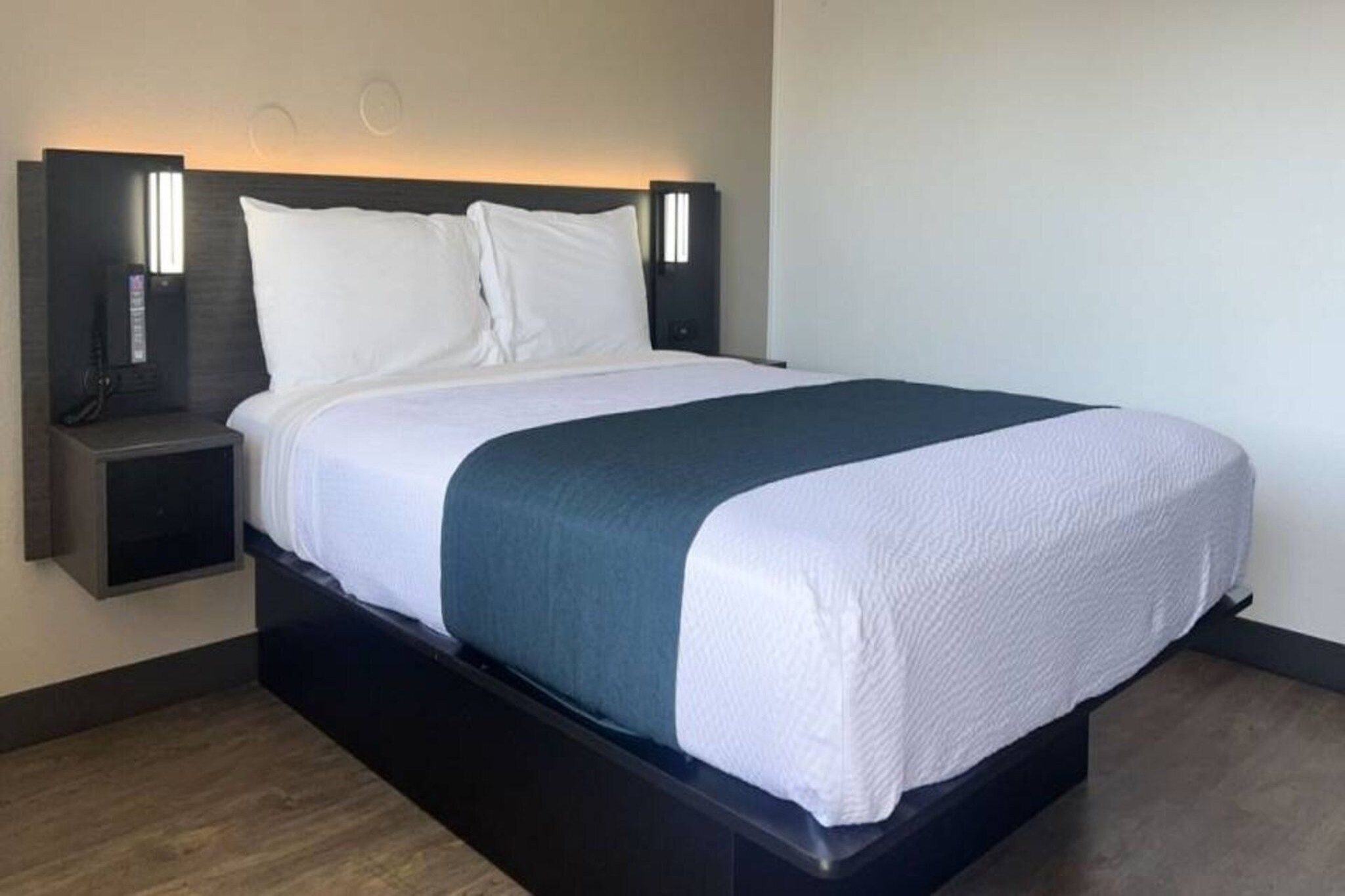 A modern hotel room with a bed, bedside tables, and wall-mounted lighting.