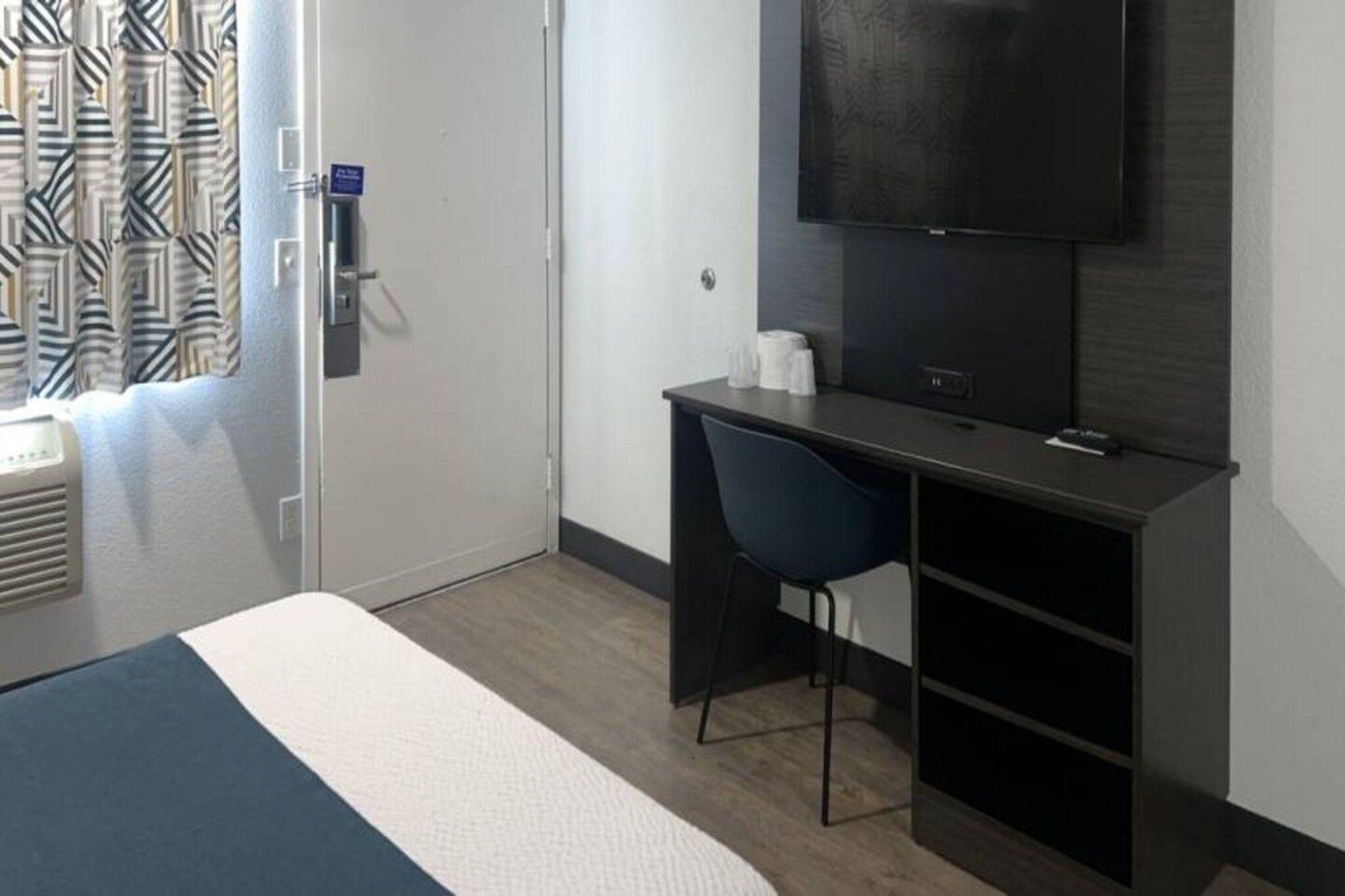 Een hotelkamer met een bed, een bureau, een stoel, een televisie en een raam met gordijnen.
