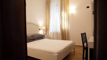 Une chambre à coucher avec un lit, une table de chevet, une lampe, une chaise et une fenêtre avec des rideaux.