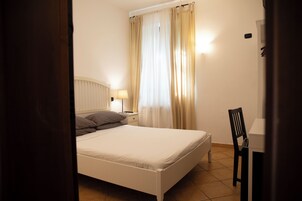 Una camera da letto con un letto, un comodino, una lampada, una sedia e una finestra con tende.