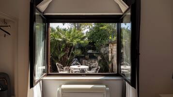Une pièce avec une fenêtre donnant sur un jardin planté de palmiers et une table entourée de chaises.
