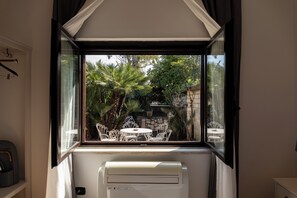 A room with a window overlooking a garden with palm trees and a table with chairs. - Mas Collection - San Bartolomeo (Bari)