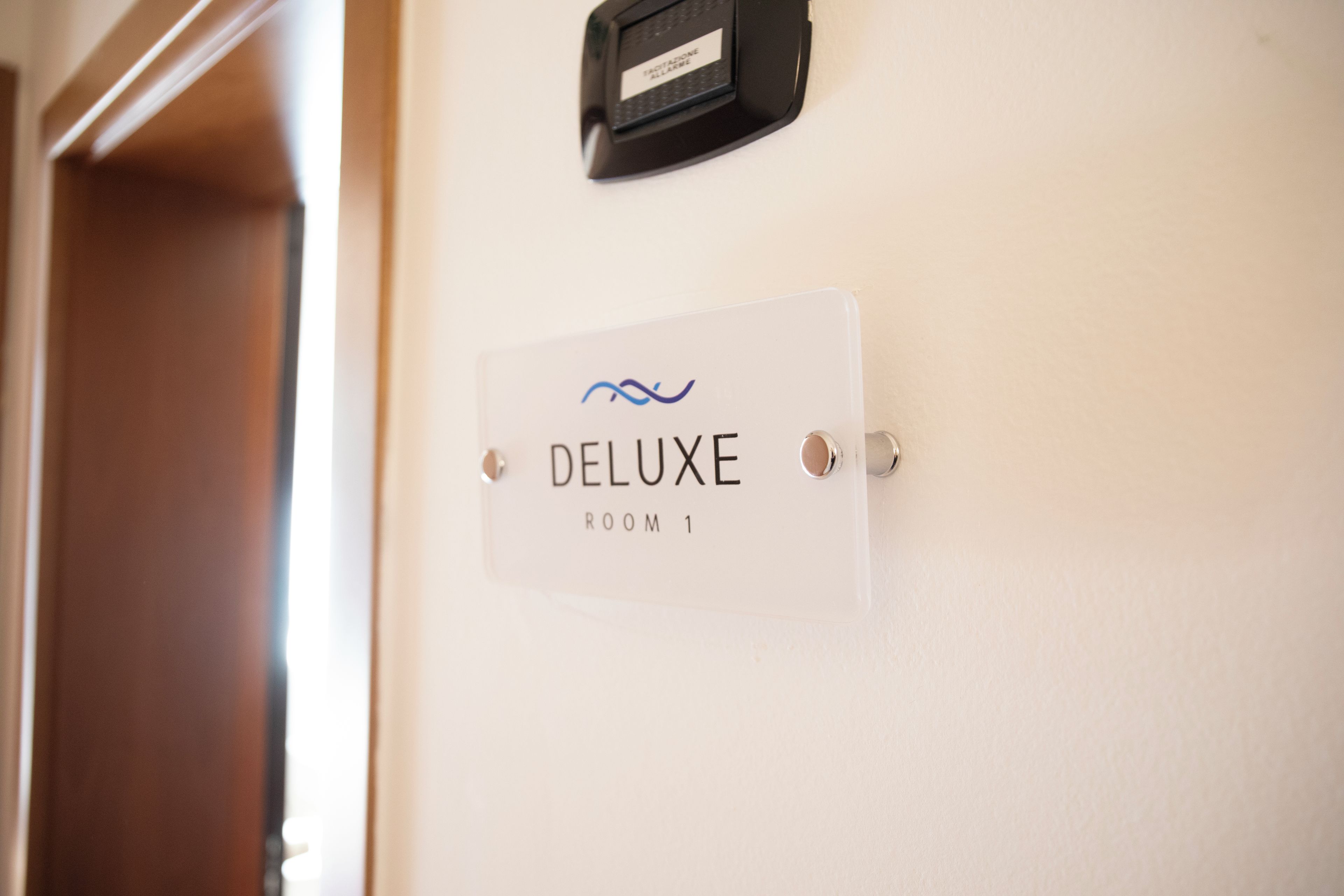 Ein Schild mit der Aufschrift 'DELUXE ROOM 1' an einer Wand, daneben ist eine Tür teilweise sichtbar.
