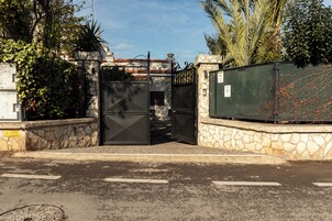 Un ingresso recintato con un muro in pietra, un cancello metallico e una recinzione a rete metallica.