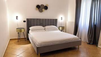 A bedroom with a bed, two bedside tables, a wall-mounted light fixture, and a window with curtains.