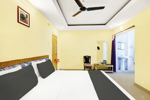 Una habitación de hotel con una cama, una silla, una mesita con una tetera y un baño visible a través de una puerta abierta.