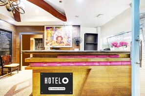 Una recepción de hotel con un cartel que dice 'HOTELO', un mostrador de madera, una silla y un cuadro en la pared.
