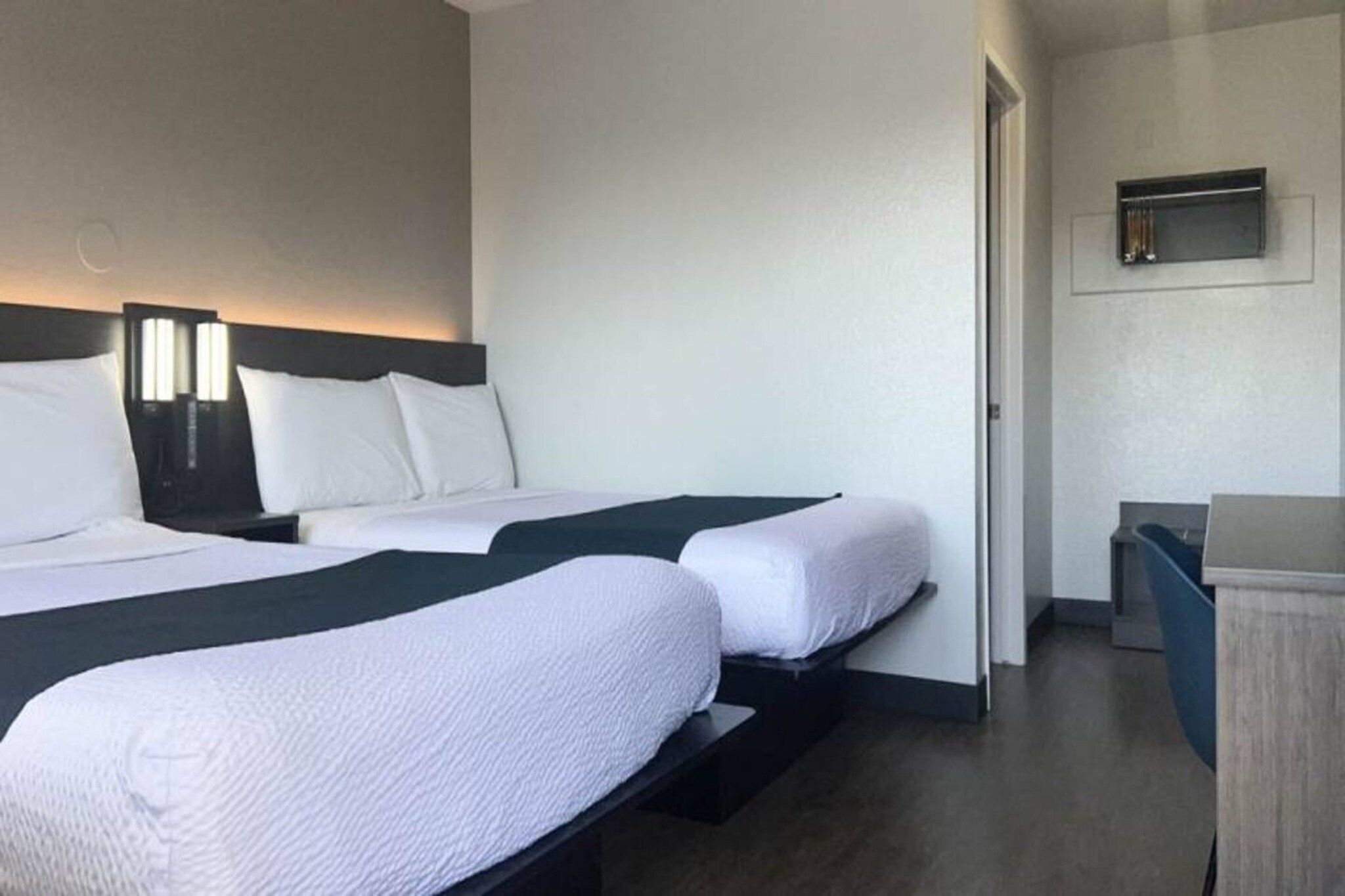 Ein Hotelzimmer mit zwei Betten, einem Schreibtisch und einem an der Wand befestigten Fernseher.
