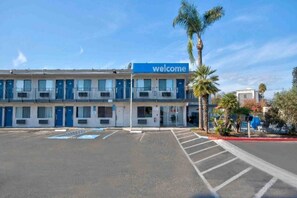 Ein zweistöckiges Motel mit einem 'Welcome'-Schild, einem Parkplatz und Palmen.
