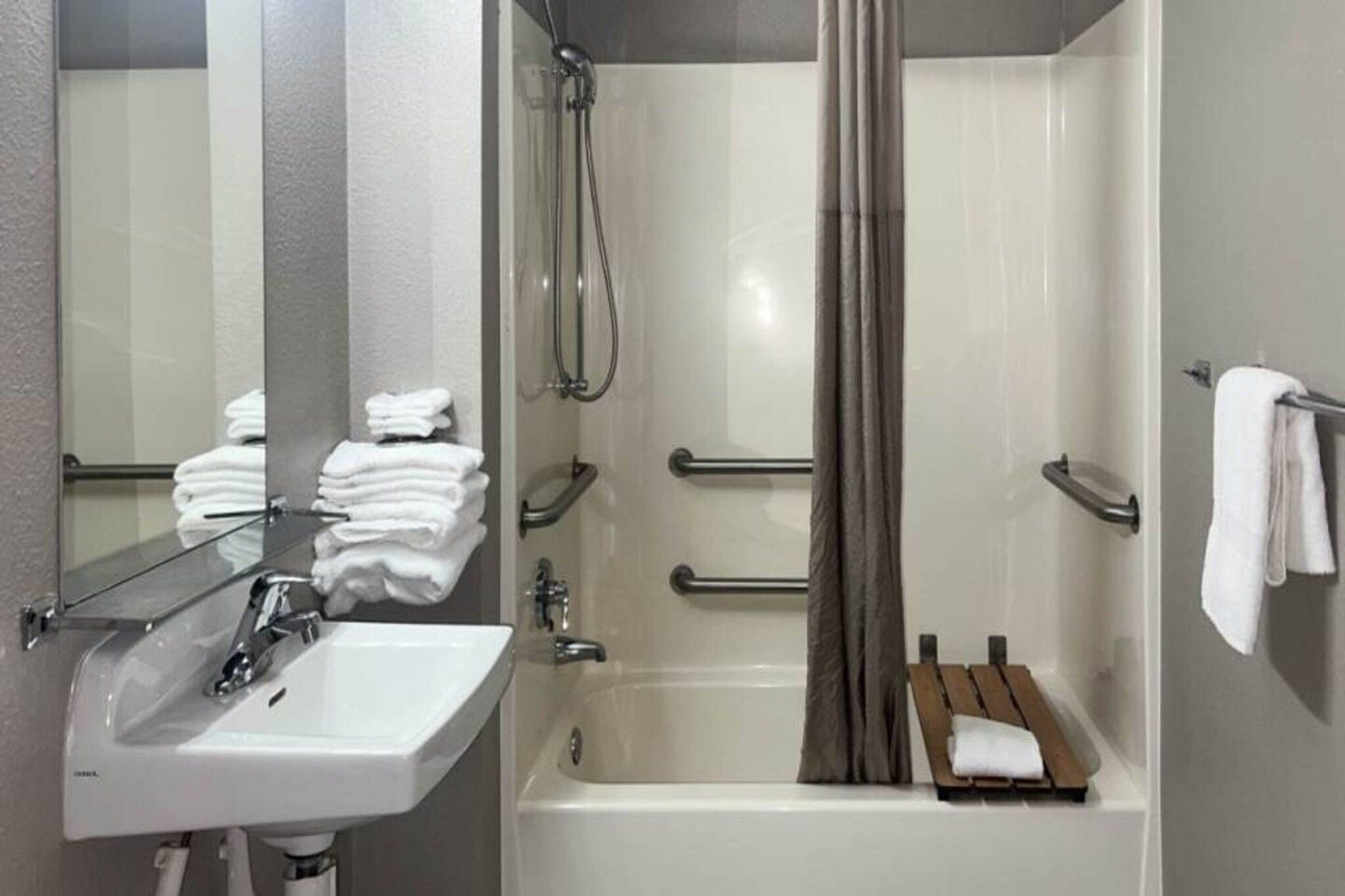A bathroom with a sink, mirror, and a shower area with a bathtub.