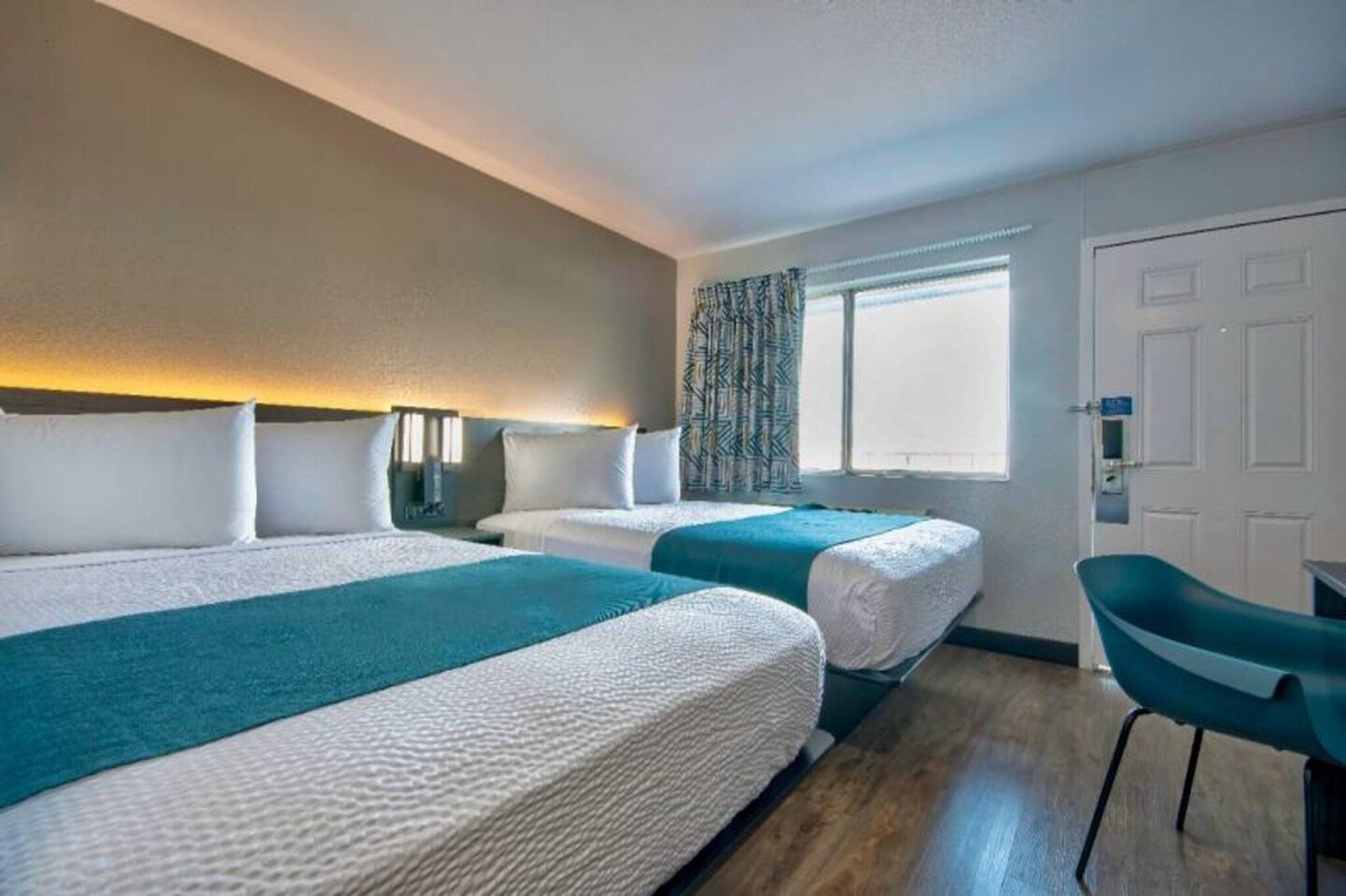 A hotel room with two beds, a desk, and a chair.
