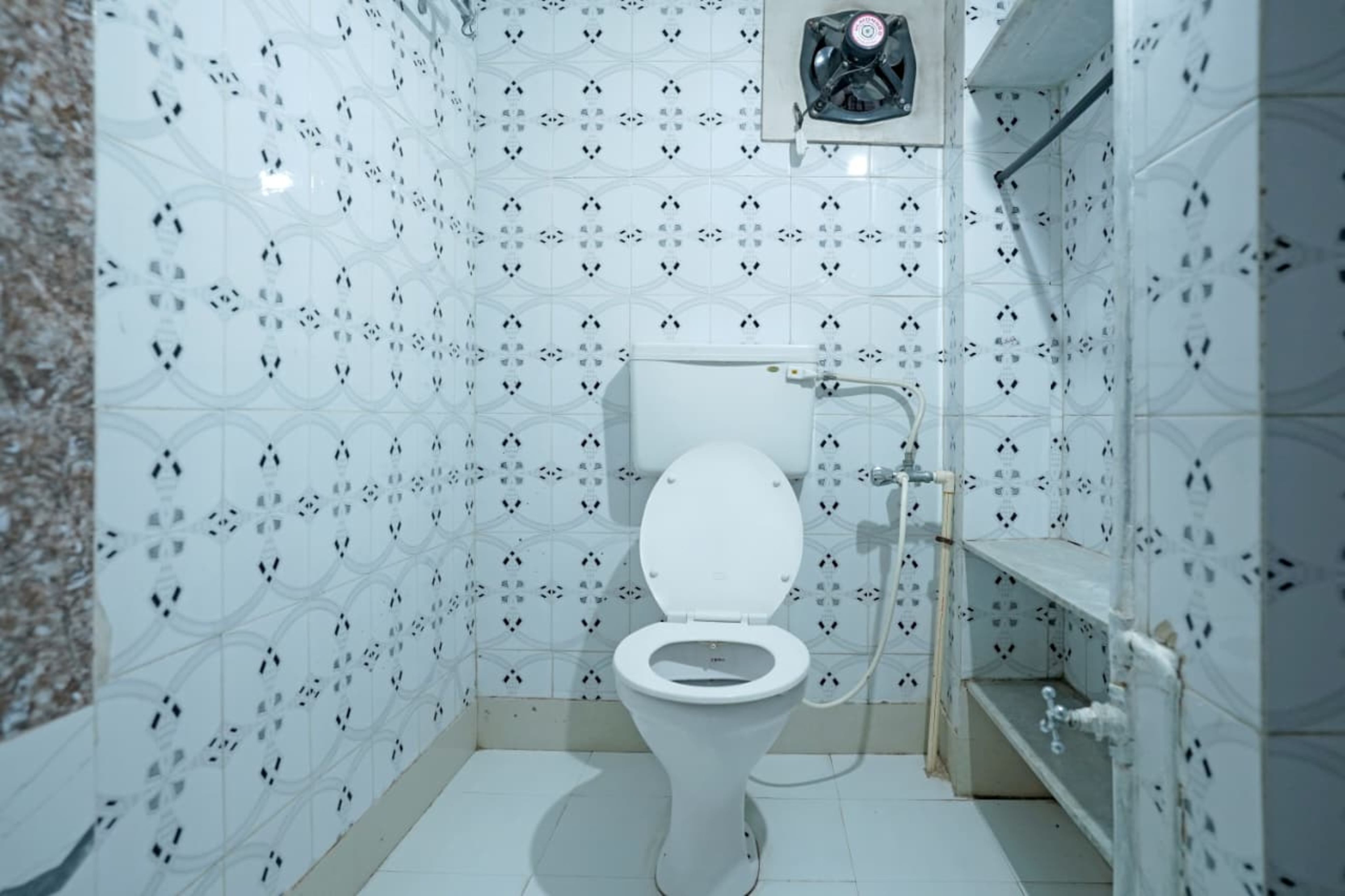 Un baño pequeño y blanco con inodoro, ducha y extractor de aire.