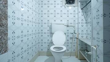 Un baño pequeño y blanco con inodoro, ducha y extractor de aire.