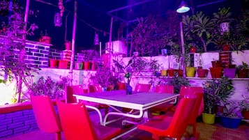 Un espacio de comedor al aire libre con una mesa y sillas, rodeado de plantas en macetas y un muro de ladrillo.