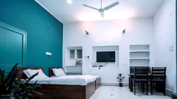 Un dormitorio con cama, ventilador de techo, televisión y escritorio con sillas.