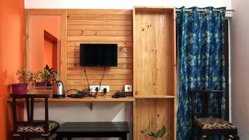 Une pièce de taille modeste, avec un téléviseur fixé au mur, un petit meuble, une bouilloire, un banc et une chaise.