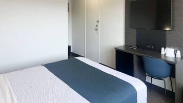 A hotel room with a bed, a desk, a chair, a television, and a wardrobe.