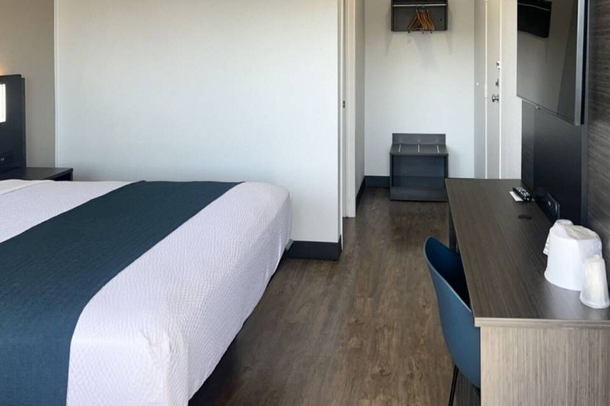 A hotel room with a bed, a desk, a chair, a small trash bin, and a mirror.