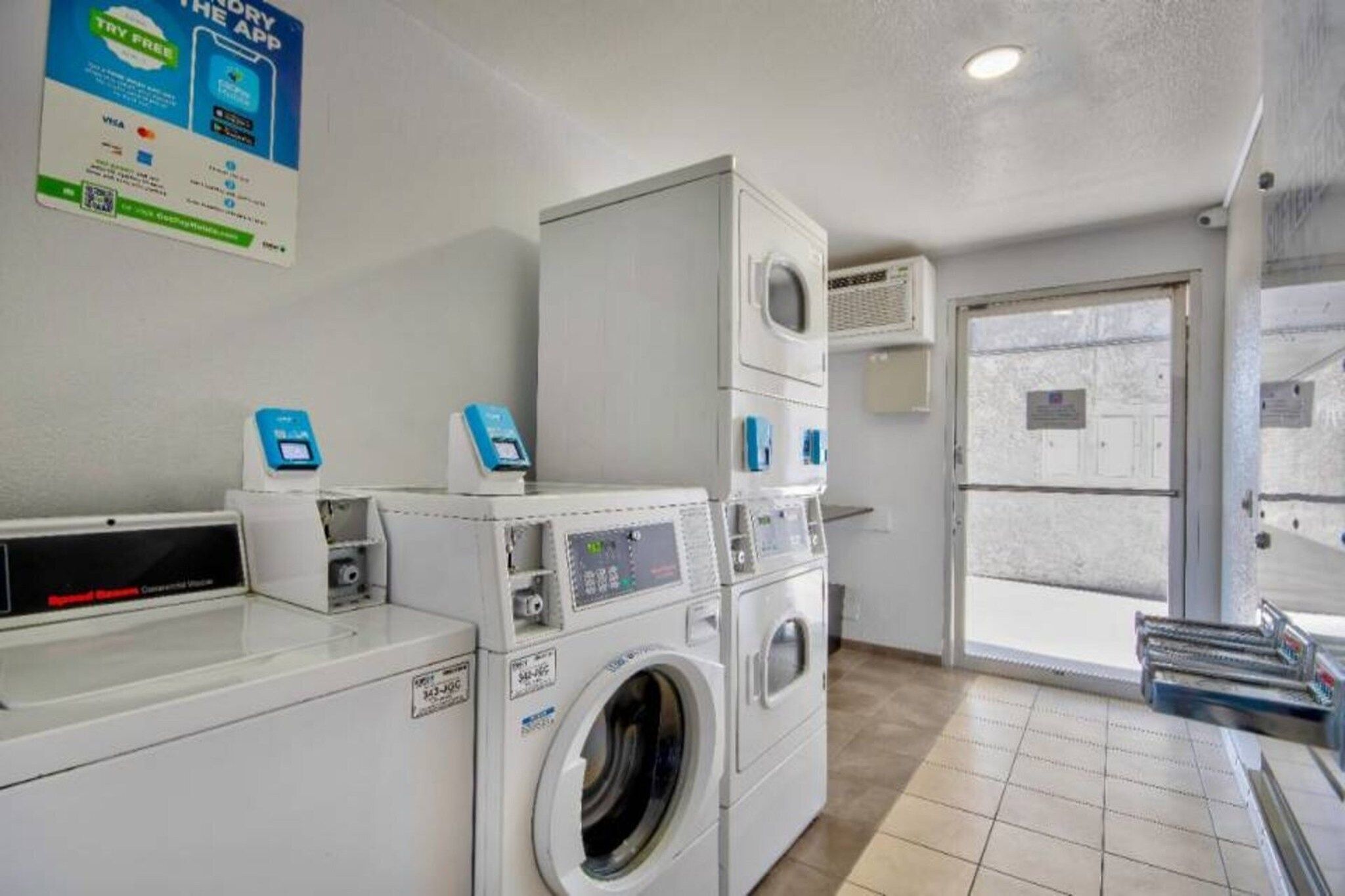 A laundry facility with stacked washers and dryers, a self-service checkout, and a door leading outside.