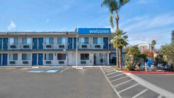 A two-story motel with a 'Welcome' sign, a parking lot, and palm trees.