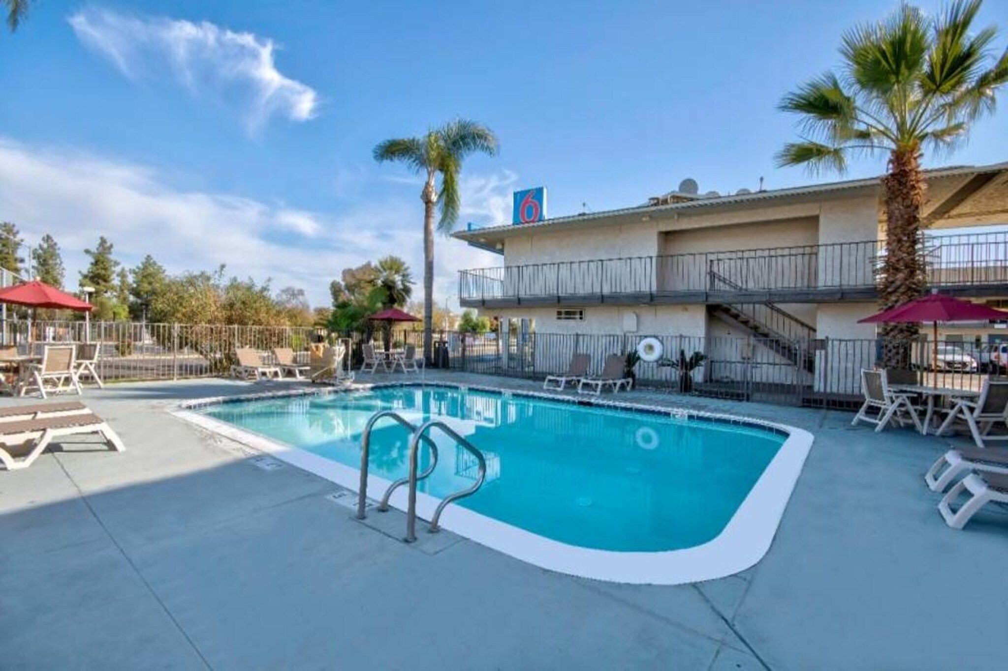 A swimming pool with lounge chairs and umbrellas, surrounded by a fenced area with palm trees.