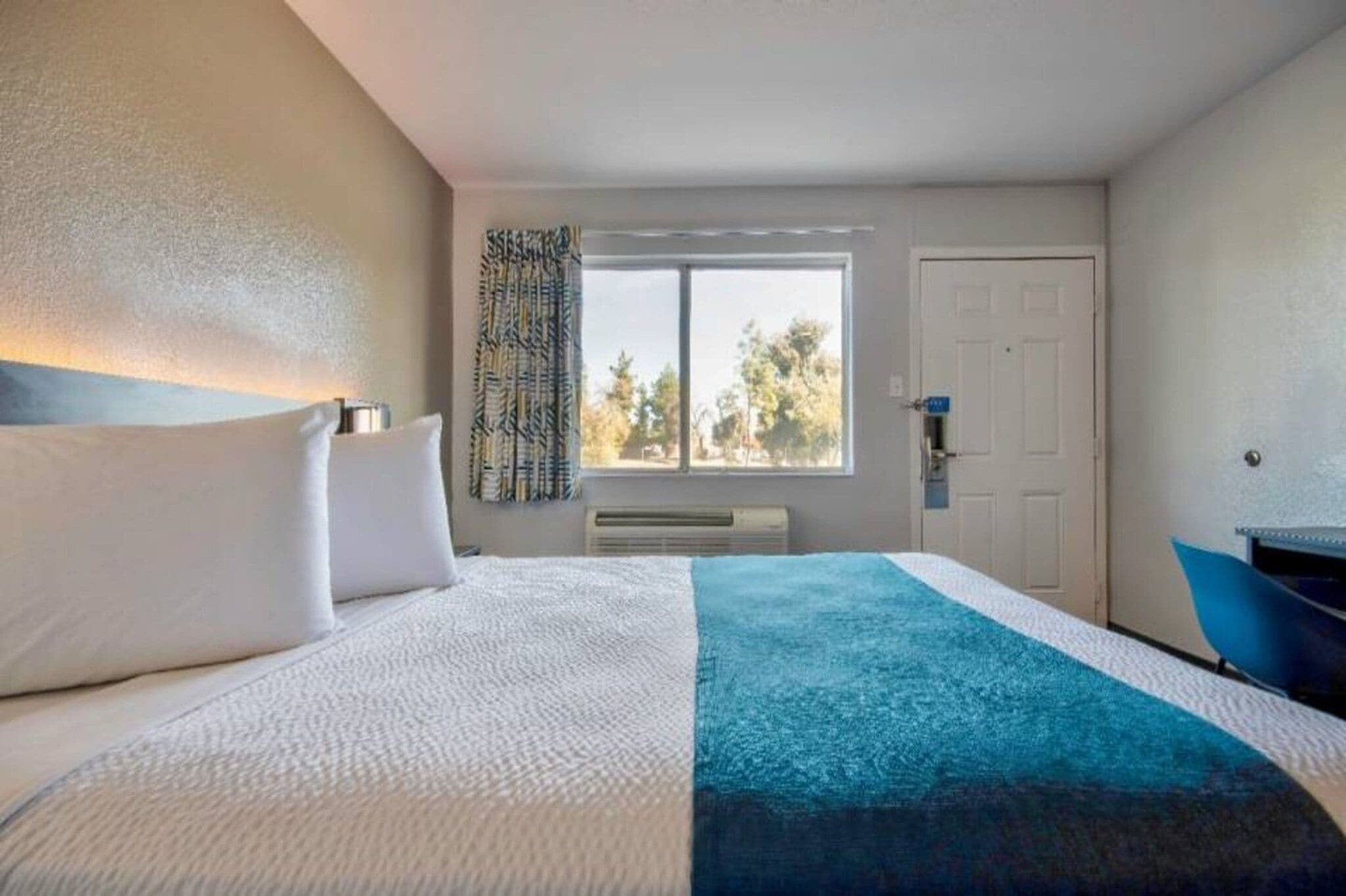 A hotel room with a bed, a window, a door, and a desk.