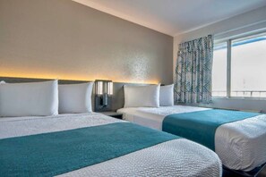 Une chambre d’hôtel avec deux lits, une table de chevet, une lampe et une fenêtre avec des rideaux à motifs.