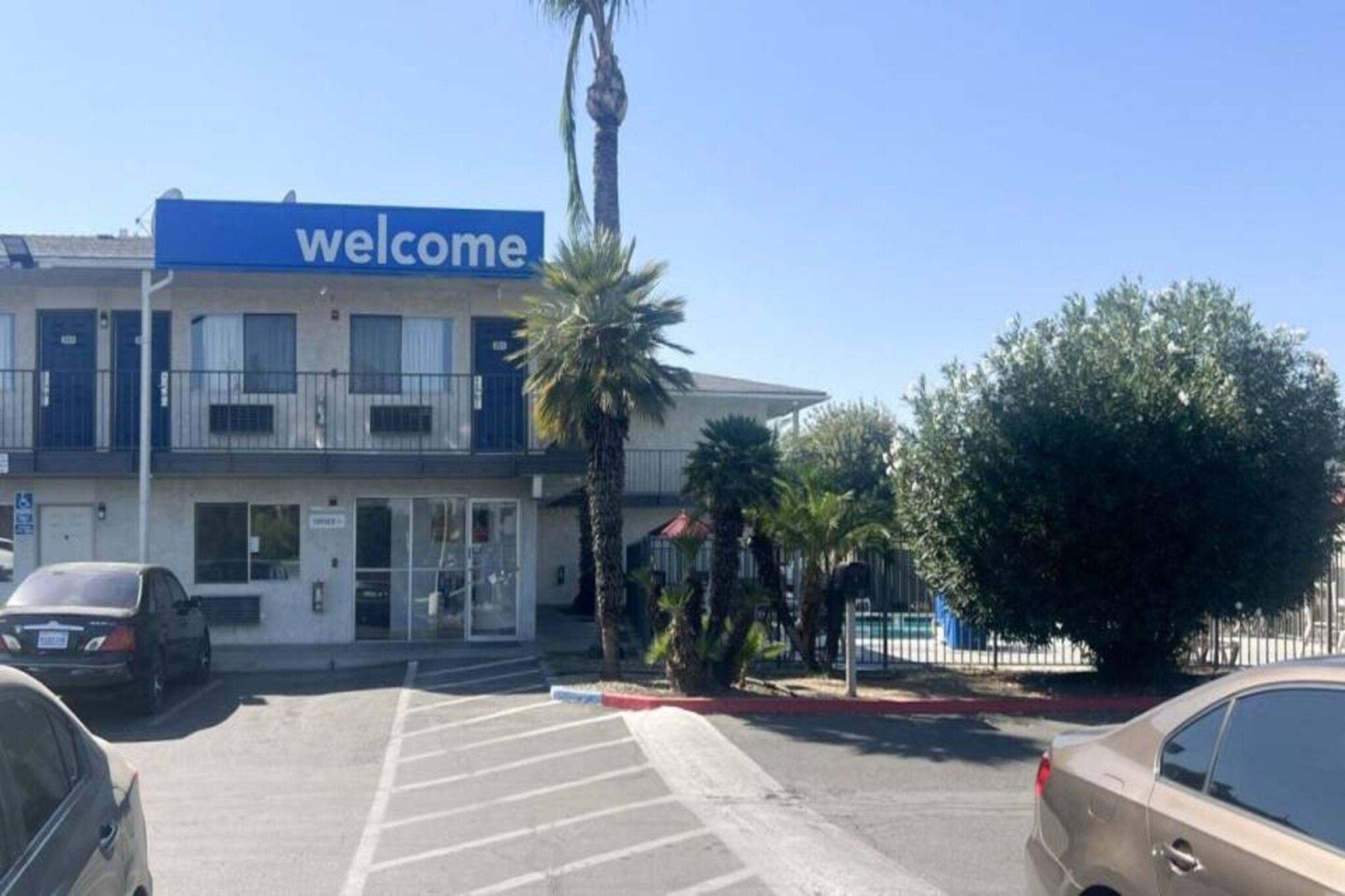 A building with a 'welcome' sign, a parking lot, and a palm tree.