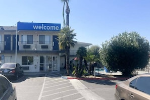 Un edificio con un letrero de 'welcome', un estacionamiento y una palmera.