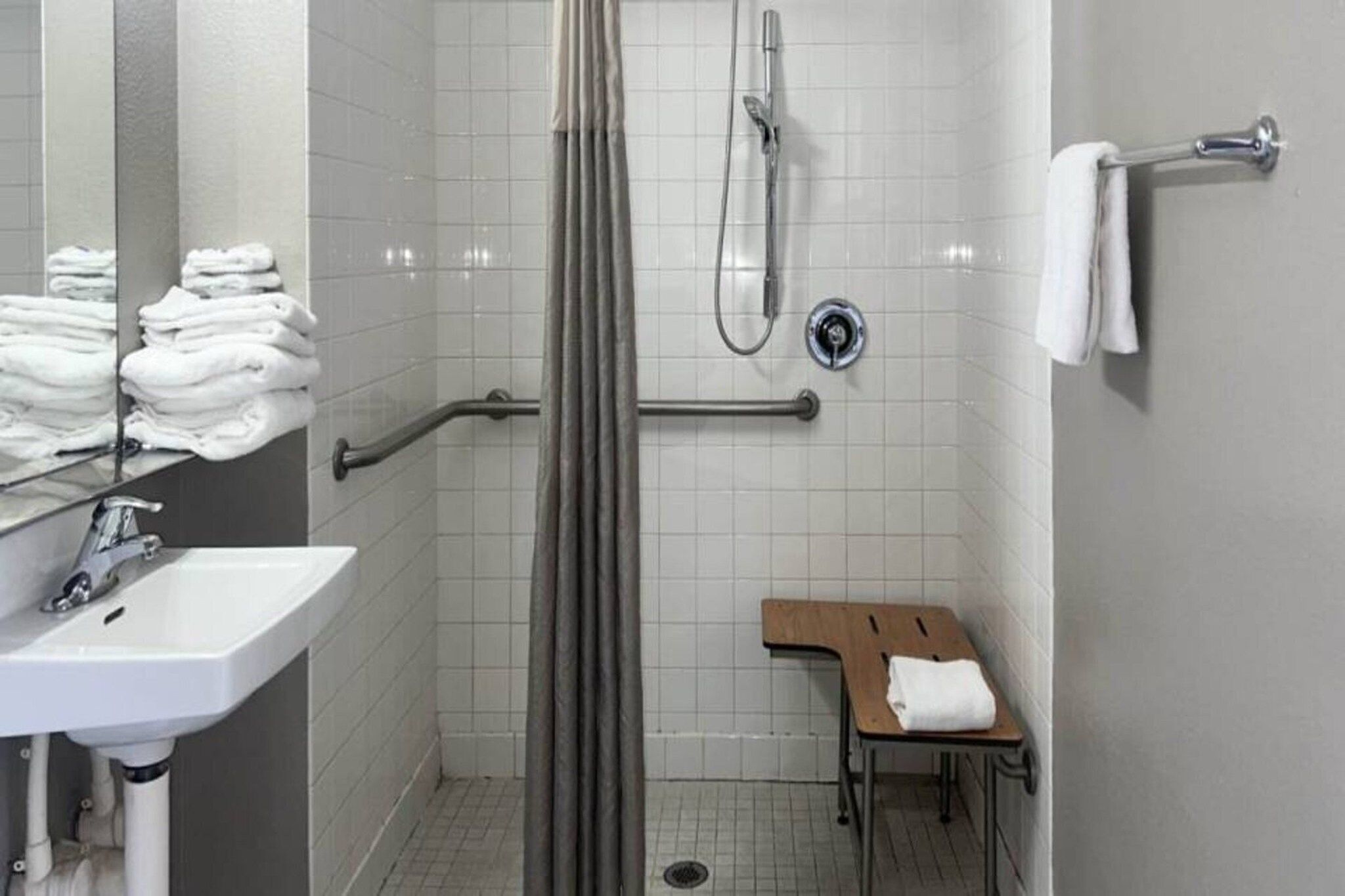 A bathroom with a shower, a sink, a towel rack, and a small wooden bench.