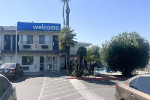 Un edificio con un cartel que dice 'welcome', un estacionamiento y una palmera.