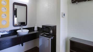 A bathroom with a sink, mirror, microwave, and a small refrigerator.