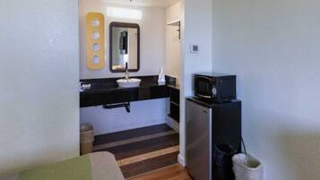 A compact kitchenette with a microwave, a sink, and a small trash bin.