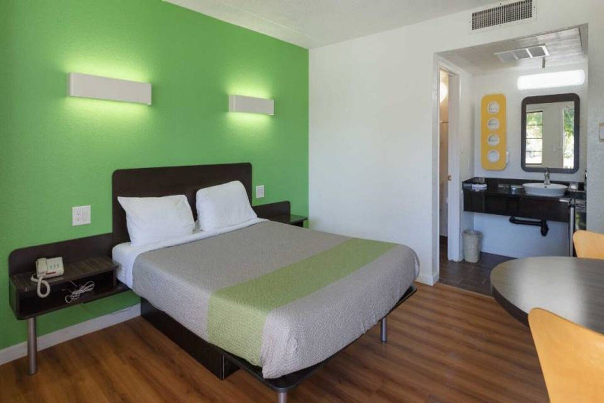 A hotel room with a bed, bedside table, and a bathroom with a sink and mirror.