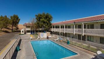 A motel with a swimming pool, outdoor seating, and a fenced area.