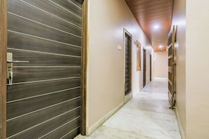 A hallway with a dark wooden door on the left, a light-colored tiled floor, and a series of doors on the right. - OYO Collection Jagannath Paradise (Varanasi)