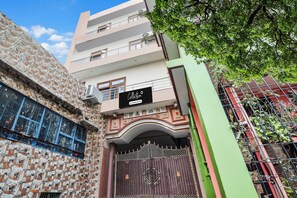 Edifici de diversos pisos amb entrada tancada per reixa, un senyal que indica servei d'una empresa i un arbre al primer terme.