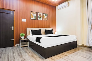 A bedroom with a bed, a nightstand, a potted plant, and a wall-mounted air conditioner. - OYO Collection Jagannath Paradise (Varanasi)