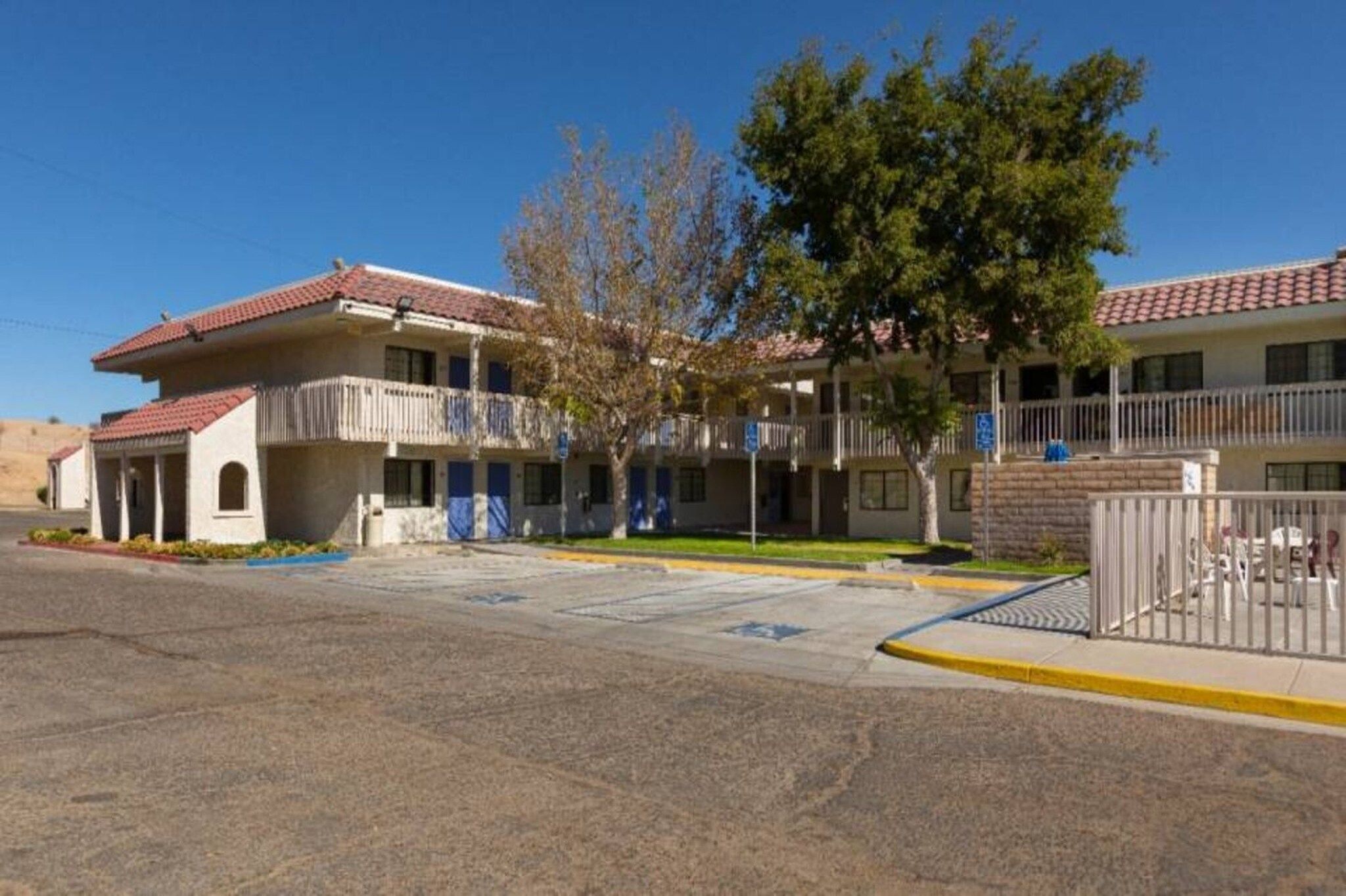 A two-story motel with a red-tiled roof, a covered parking area, and a fenced courtyard.