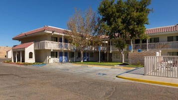 A two-story motel with a red-tiled roof, a covered parking area, and a fenced courtyard.
