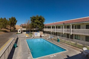 Un motel con piscina, mobiliario exterior y zona vallada.