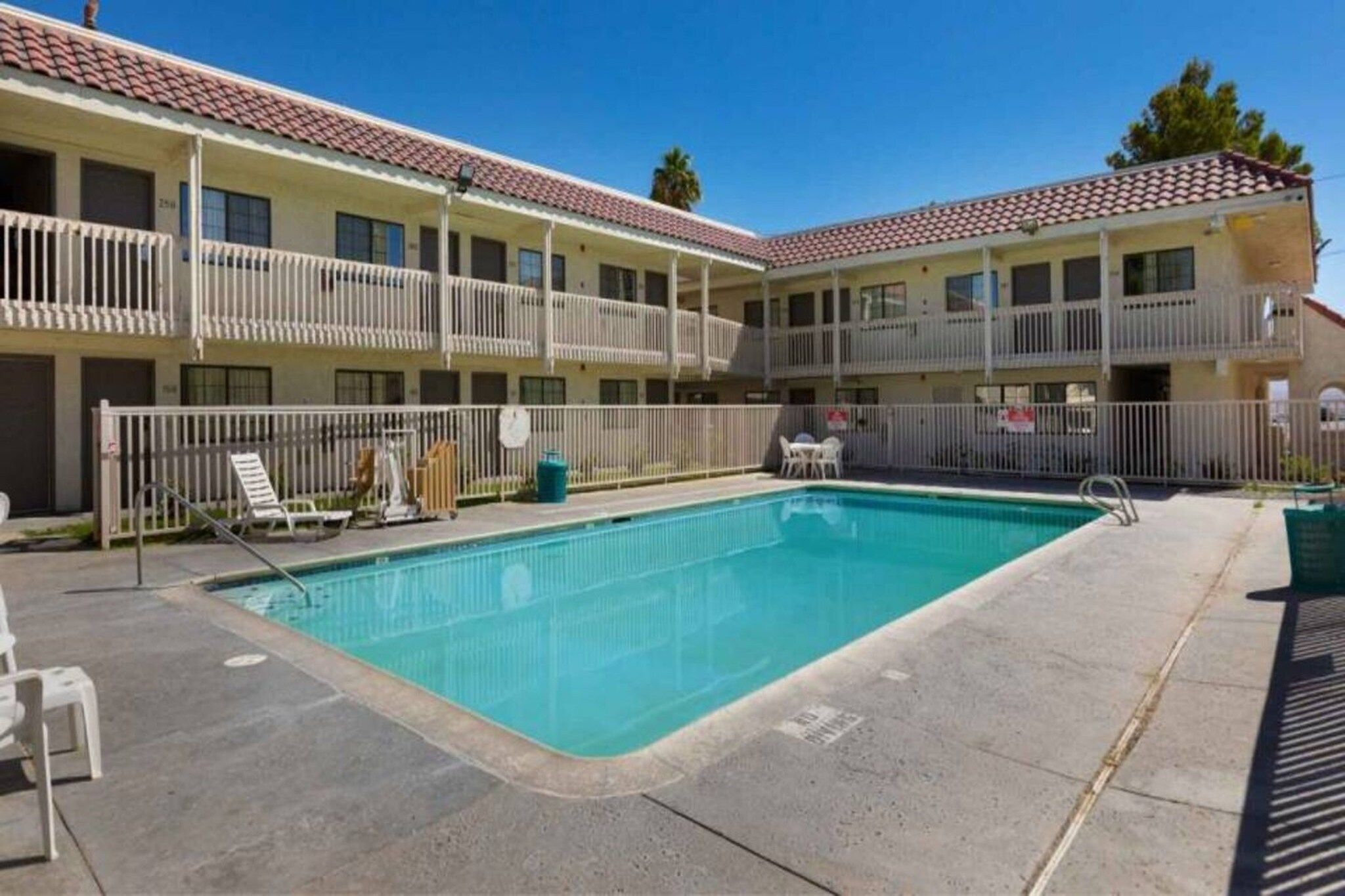 A hotel with a swimming pool, outdoor seating, and a fenced balcony area.