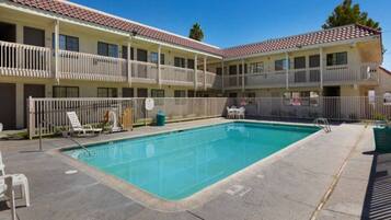 A hotel with a swimming pool, outdoor seating, and a fenced balcony area.