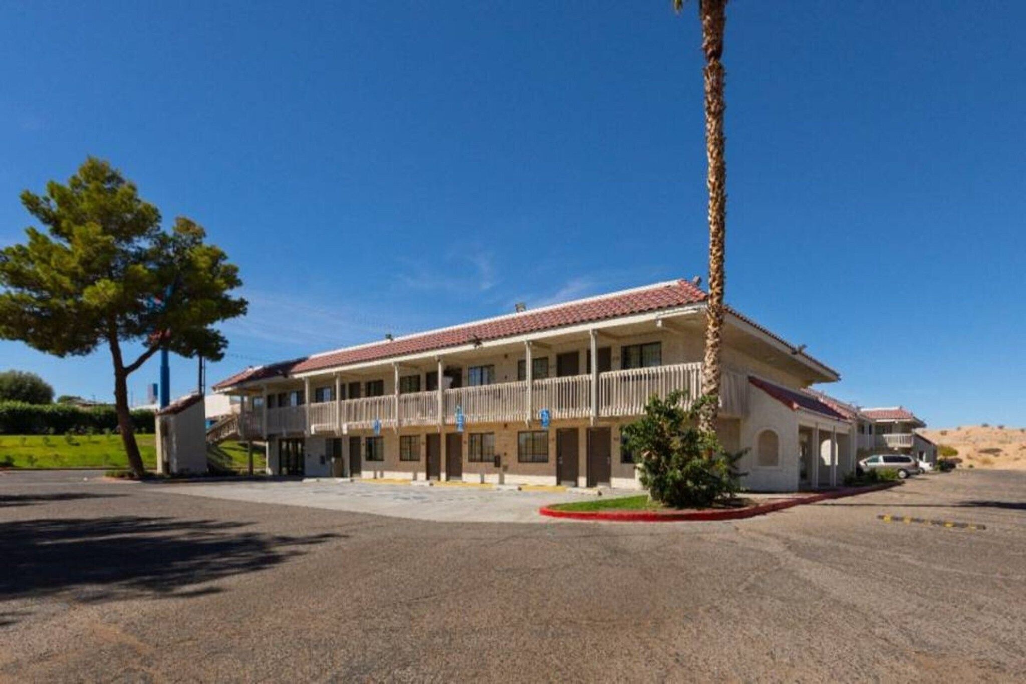 A two-story building with a balcony, a covered parking area, and a clear sky.