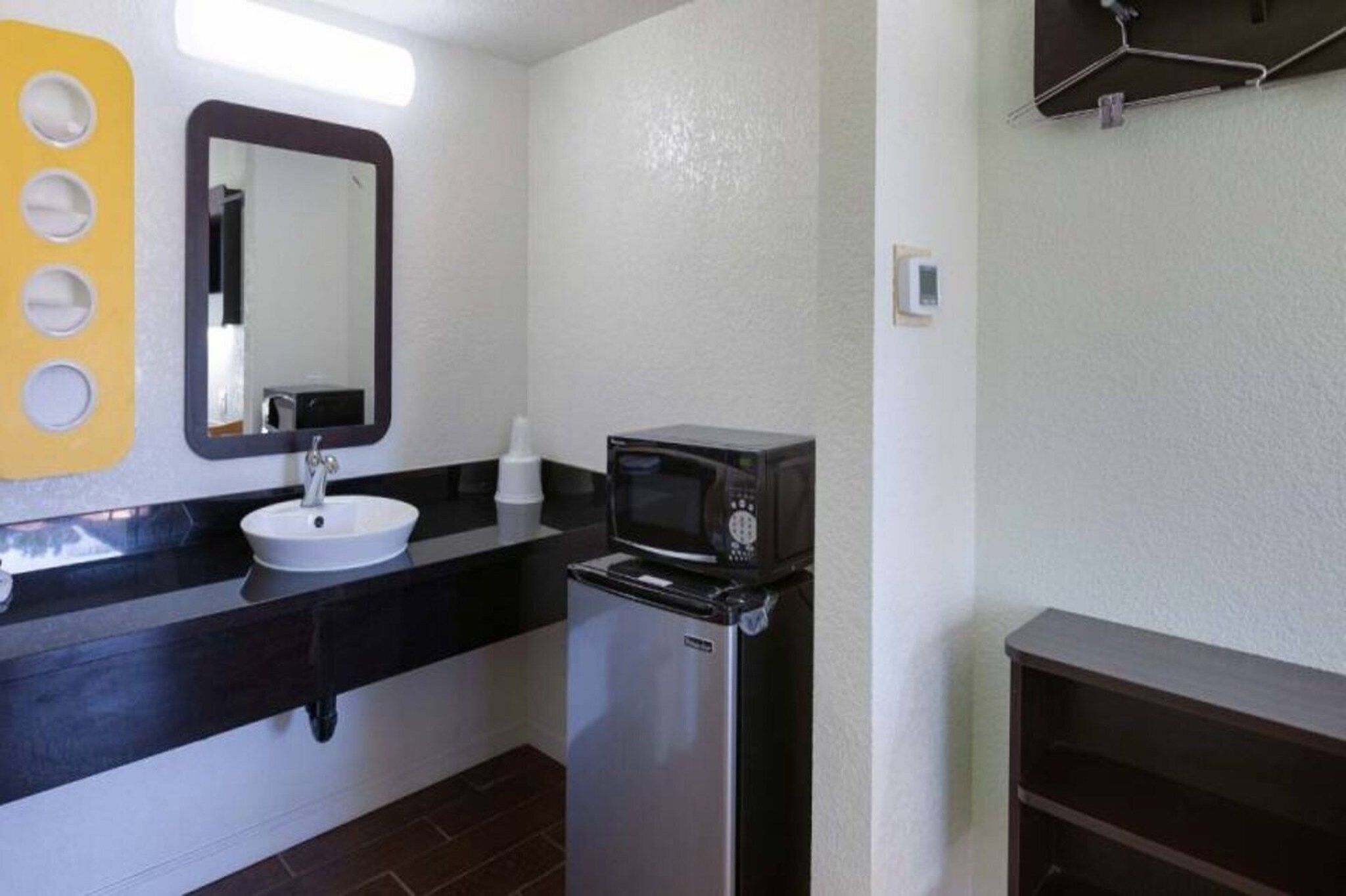 A bathroom with a sink, mirror, microwave, and a small refrigerator.