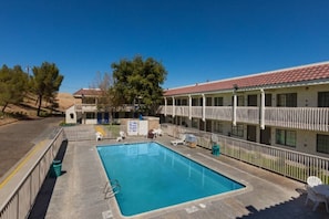 A motel with a swimming pool, outdoor seating, and a fenced area.