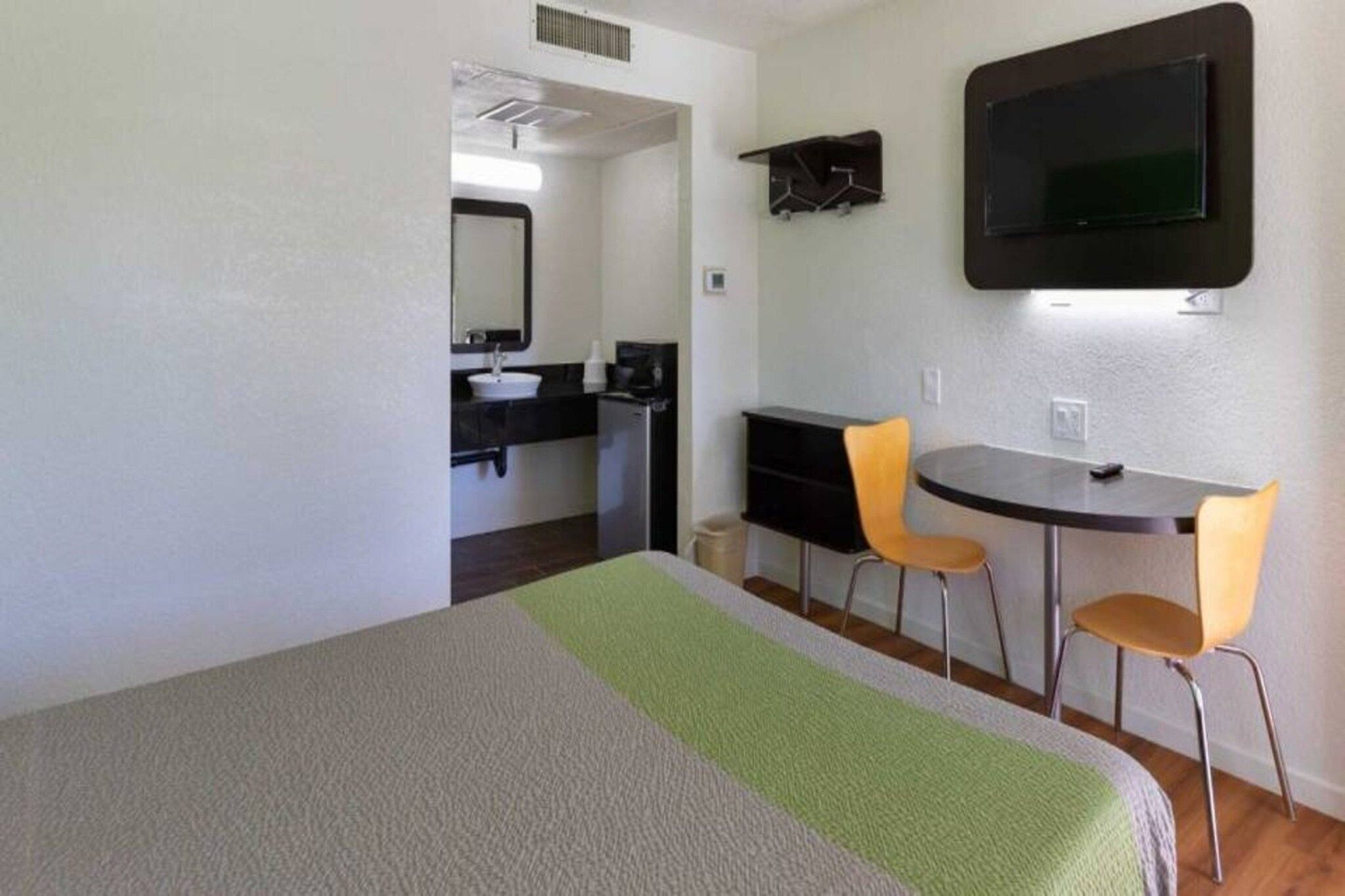 A room with a bed, a desk, two chairs, a television, and a bathroom.
