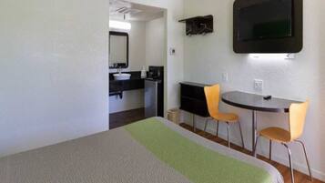A room with a bed, a desk, two chairs, a television, and a bathroom.