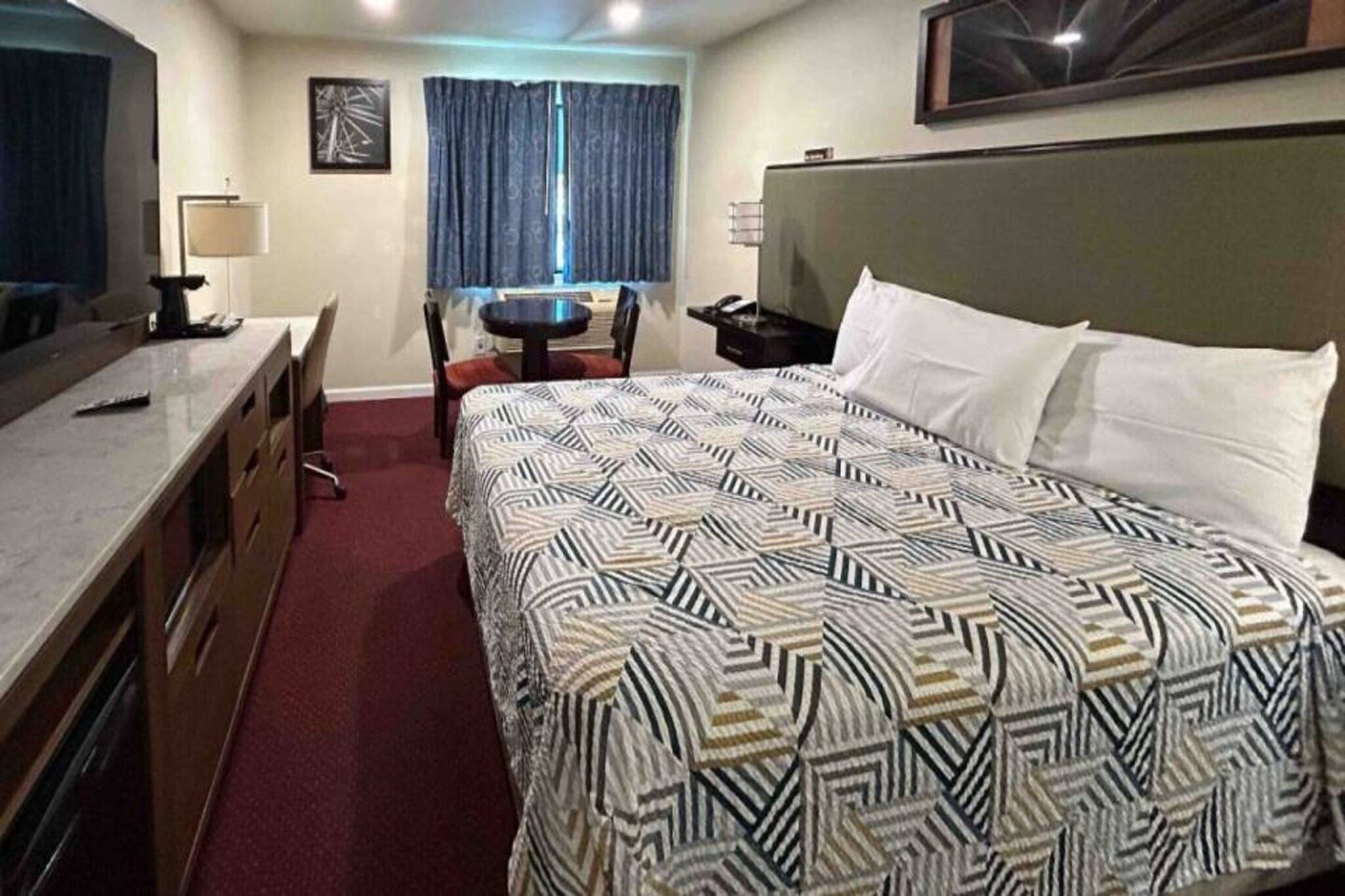 Une chambre d’hôtel équipée d’un lit, d’un bureau, d’une chaise, d’une télévision et d’une fenêtre avec des rideaux.